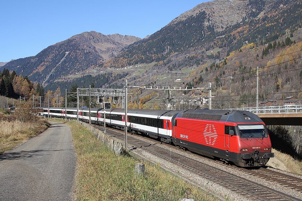Red Re 460 locomotive hauling a rake of white single-deck EuroCity coaches with red doors through the Leventina valley