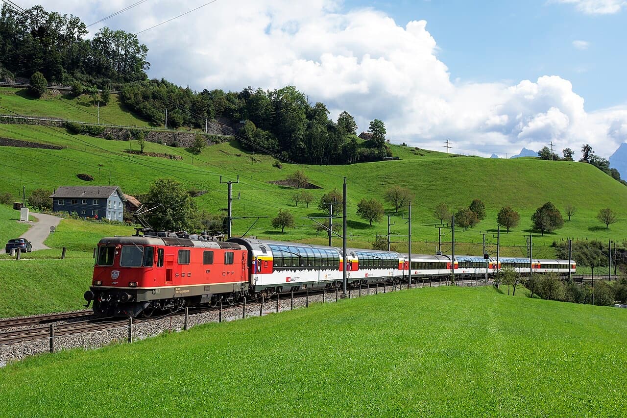 Red SBB Re 420 locomotive hauling the Gotthard Panorama Express with glass-roofed panorama coaches through green hills