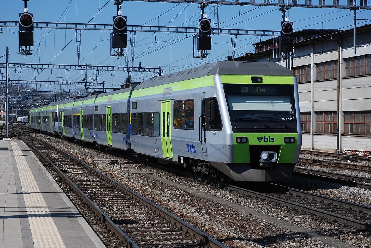 Two coupled BLS RABe 525 NINA low-floor units in silver and green arriving at a station