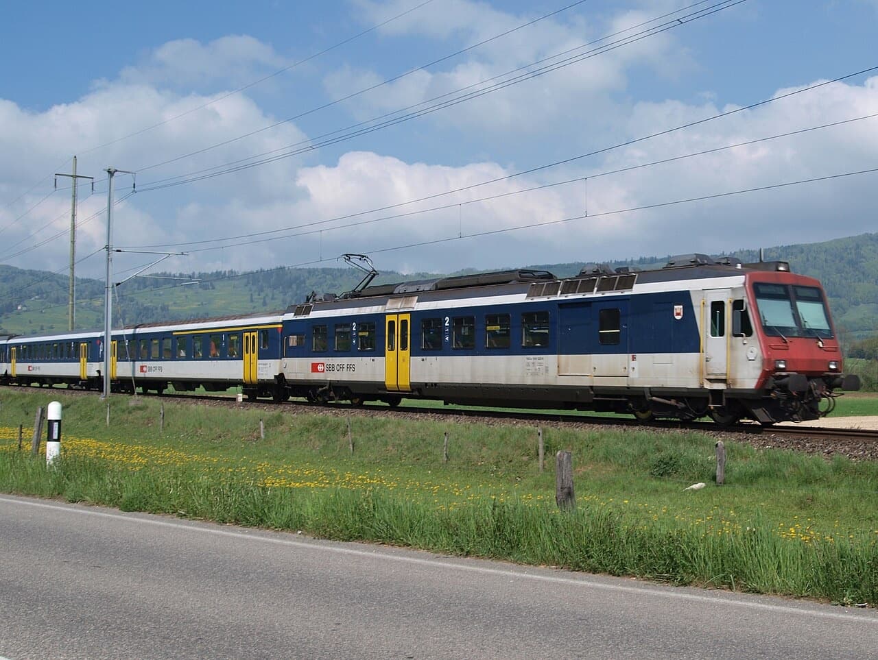 NPZ regional train with red cab front and blue-grey-white sides with yellow doors, running through fields